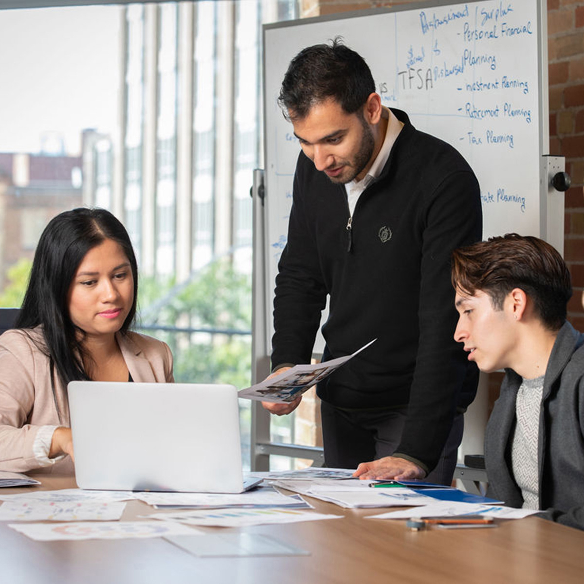 A photo of three post-graduate students around a desk working on a project