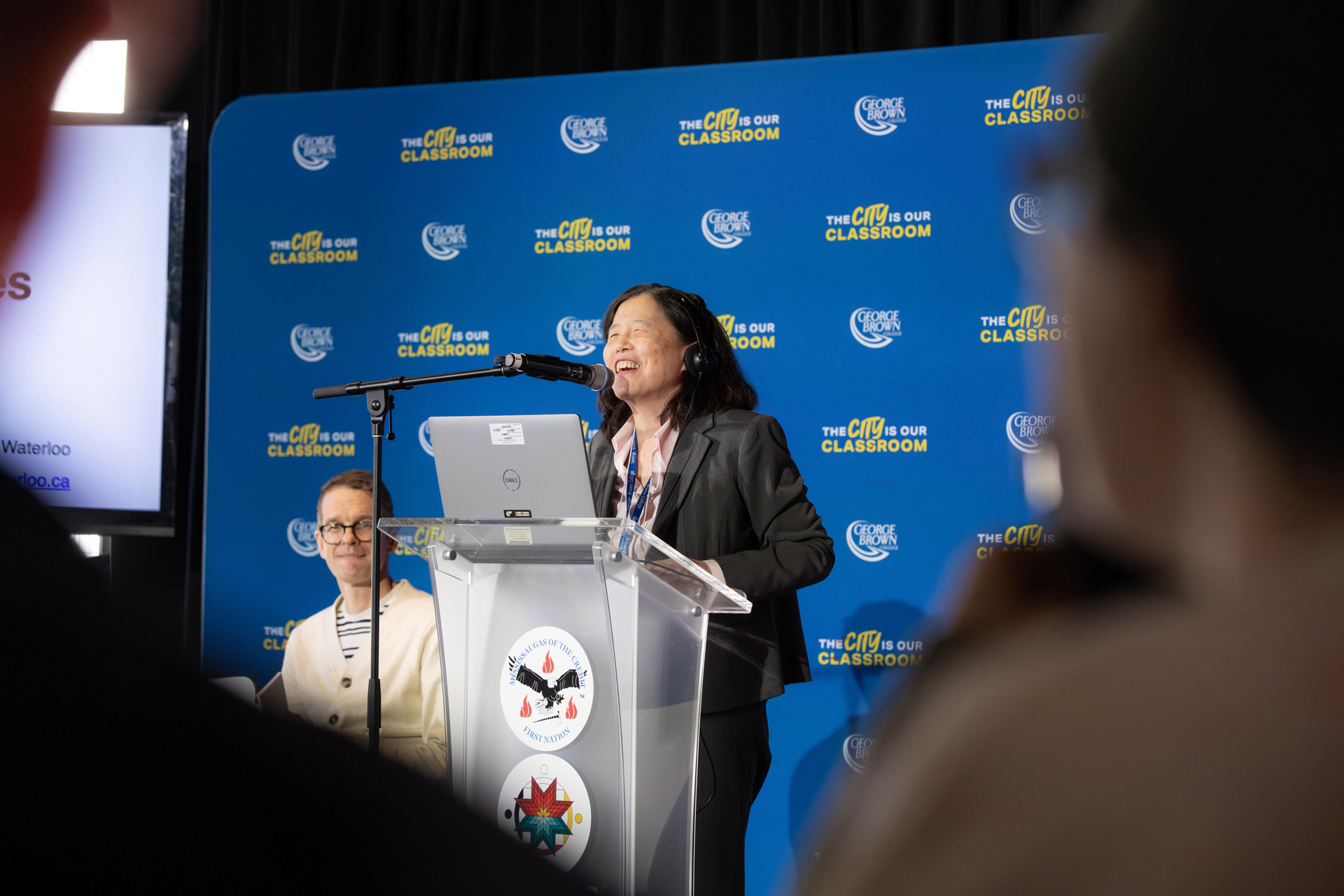 A woman stands at a podium speaking into a microphone