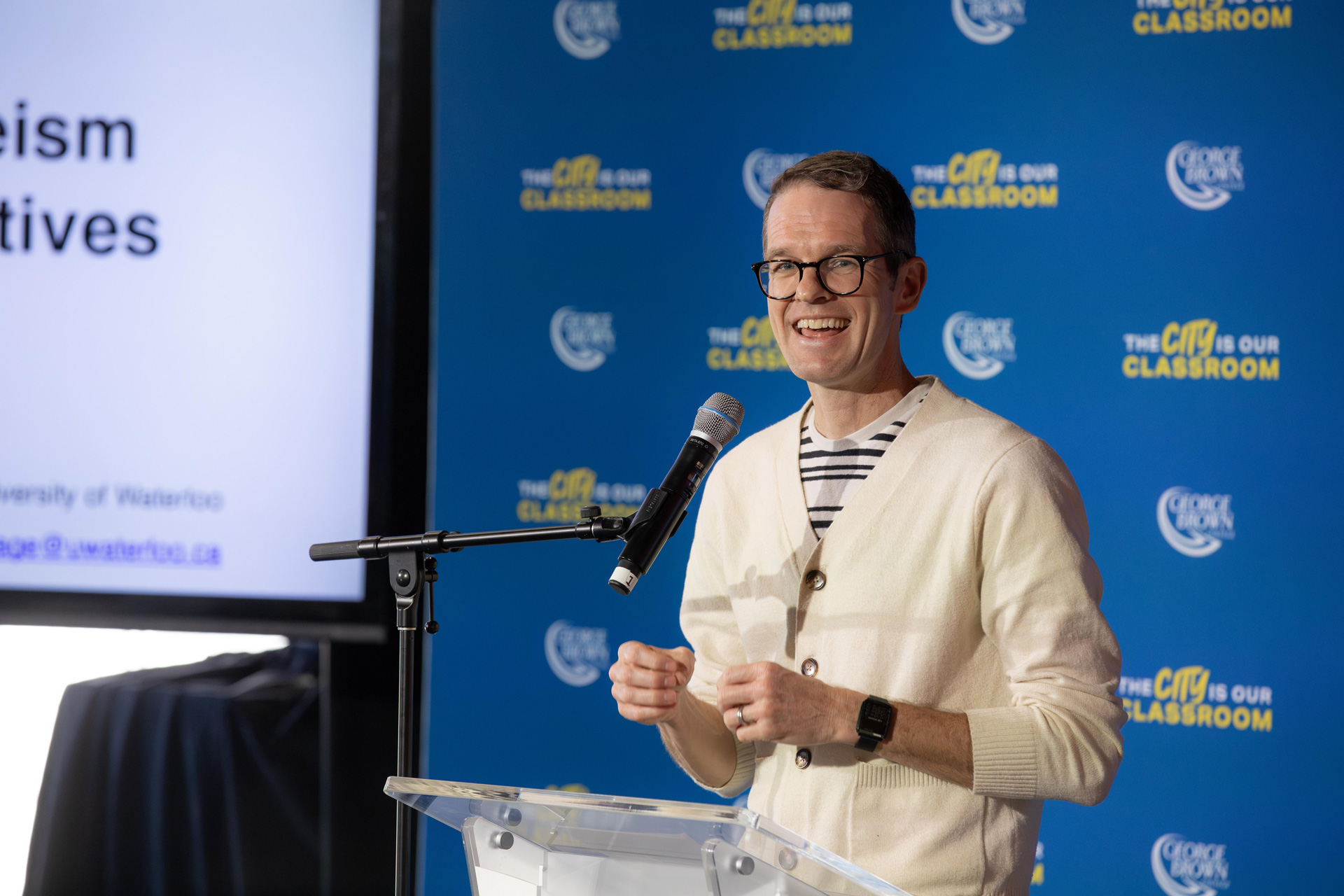 A man smiles while standing at a podium with a microphone