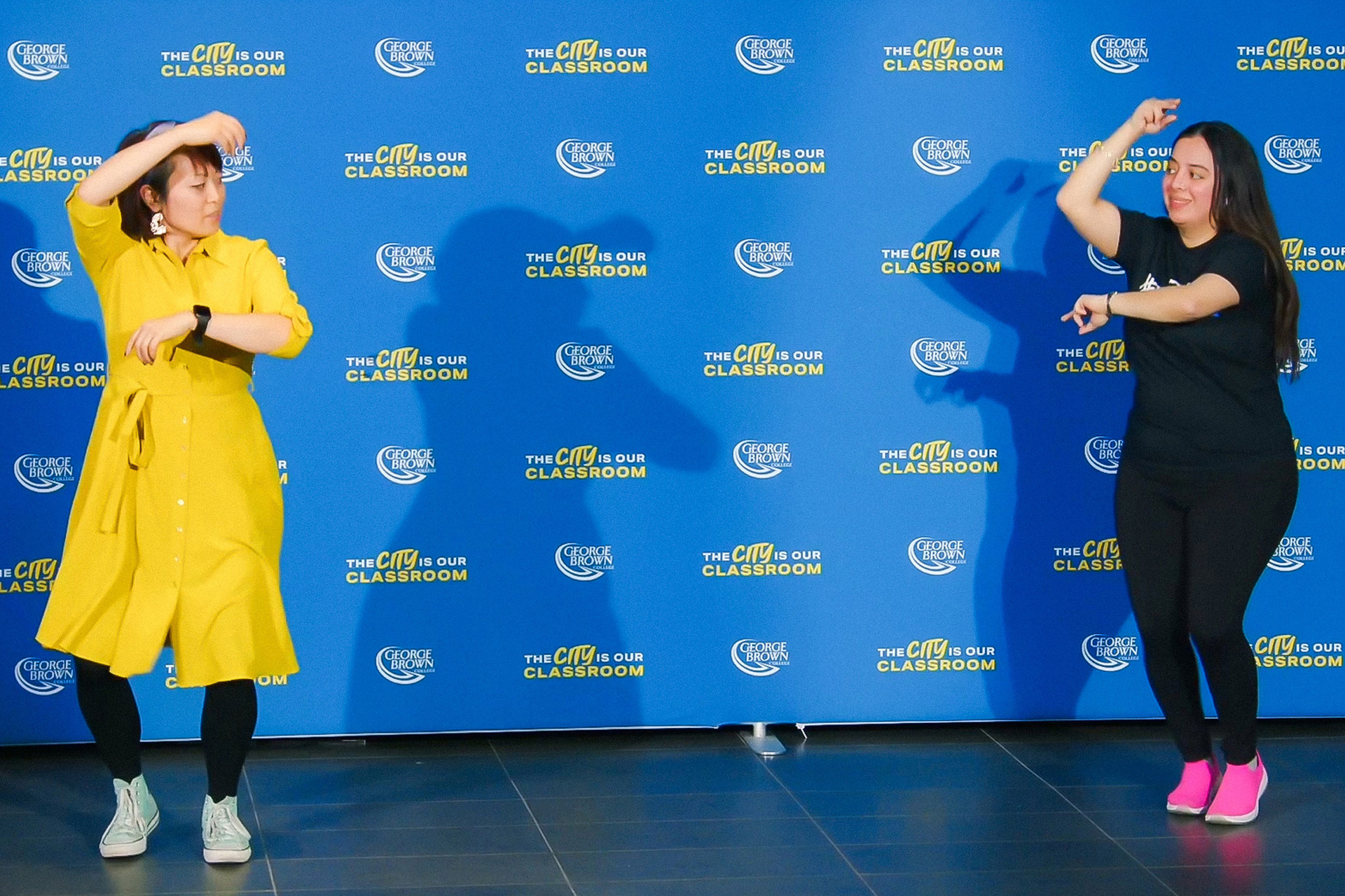 Two students dance in front of a blue background