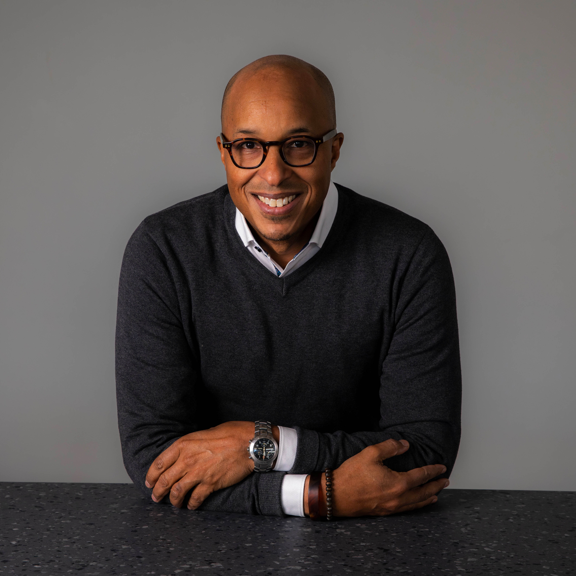 Man in a black sweater and collared shirt with arms crossed smiles