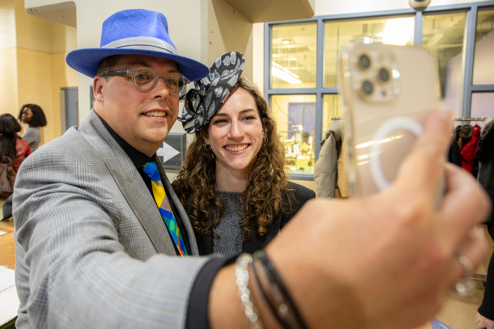 A man and woman smiling together while taking a selfie with a cell phone in a bright indoor setting.