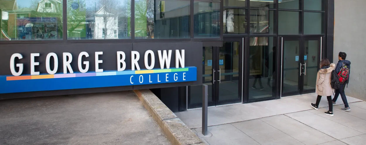 A male and female student walking towards a Casa Loma campus entrance near a George Brown College sign.
