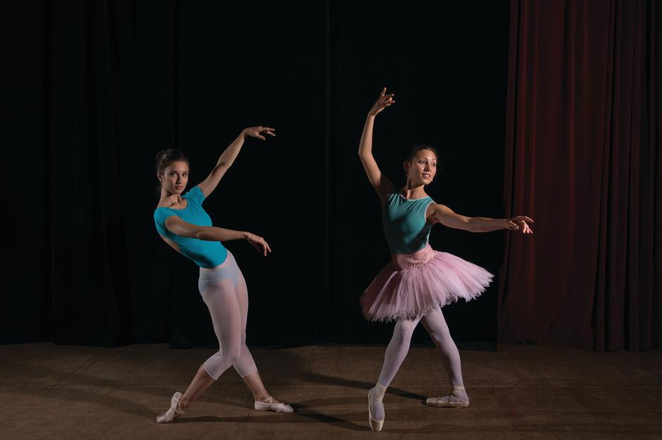 Two female dance program students are performing on stage dressed up as ballerinas.