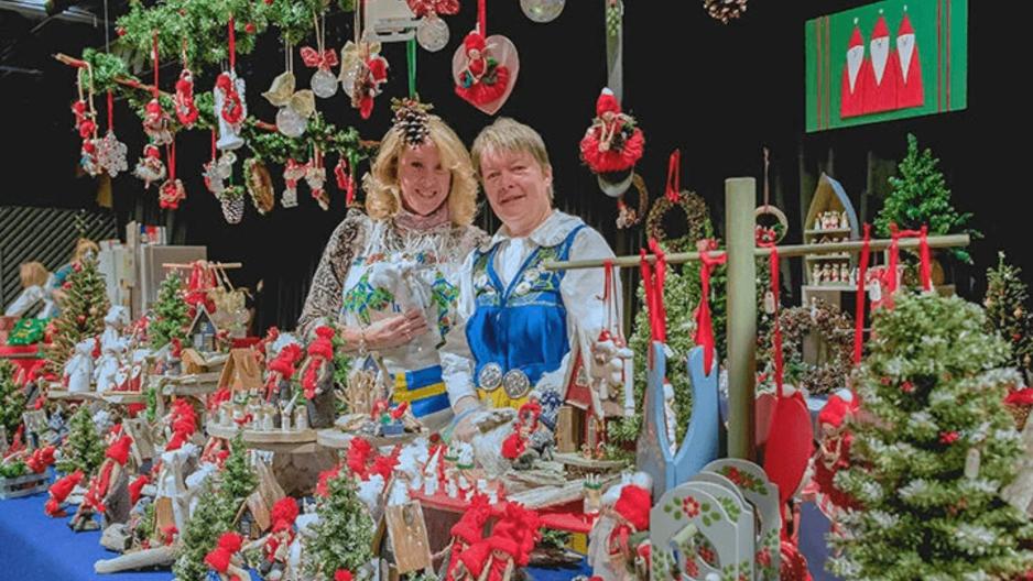 Two women stand behind a table decorated with Swedish and Christmas items.