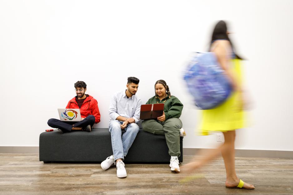 Three seated students on a bench looking at their laptops