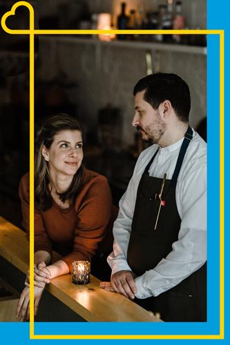 A woman looks lovingly at a man in a white shirt and black apron