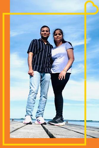 Two people stand on a pier in front of a lake with a bright blue sky